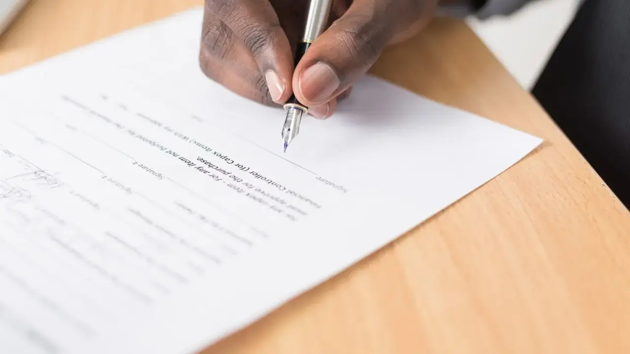 Main d'une personne signant un document, peut-être une liste pour une maison d'édition à compte d'éditeur.