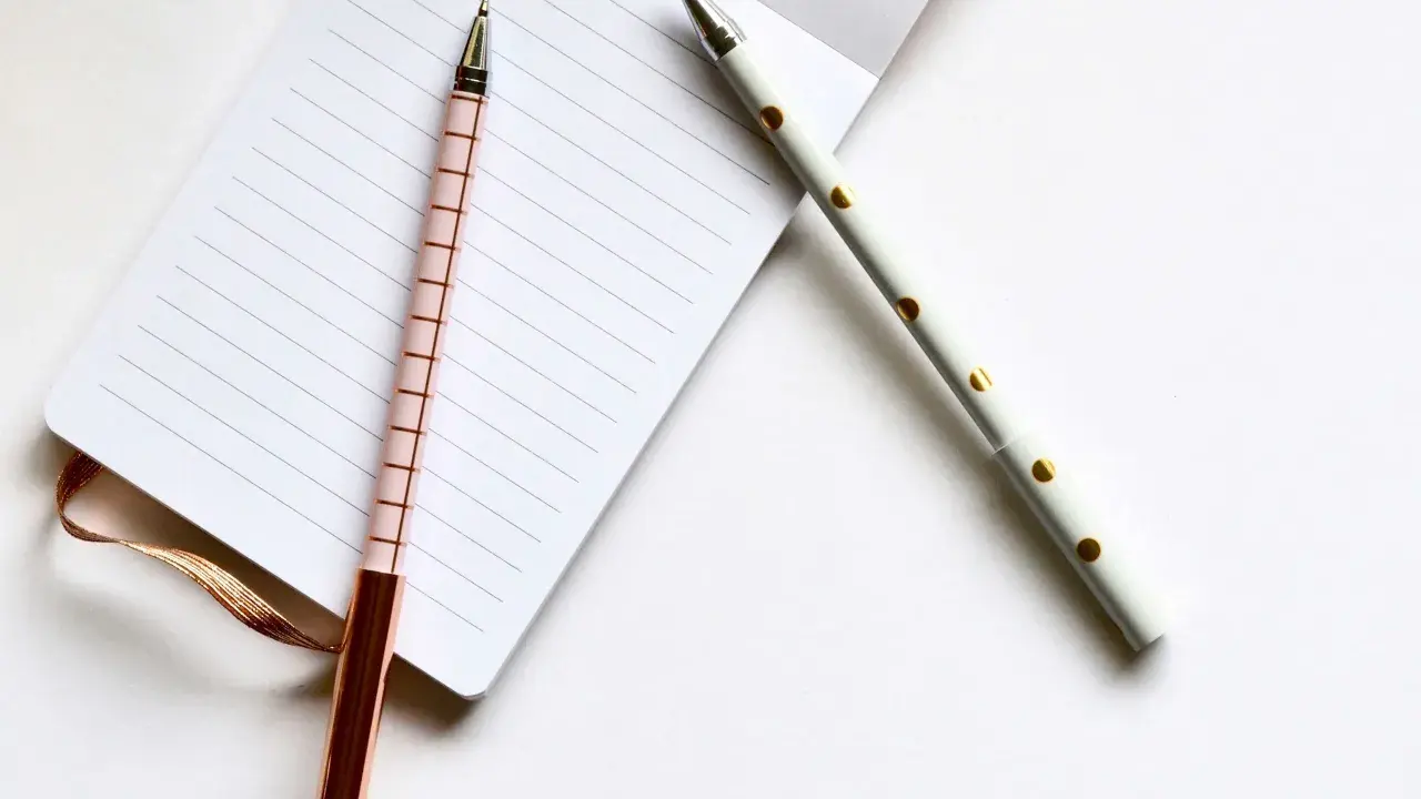 Deux stylos élégants, un rose à carreaux et un blanc à pois dorés, reposent sur un carnet ligné, prêts pour les éditions Balland manuscrit.