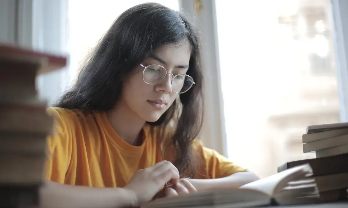 Jeune femme aux lunettes, plongée dans l'étude. Une pile de livres à côté, elle semble faire une analyse linéaire de son éducation sentimentale.