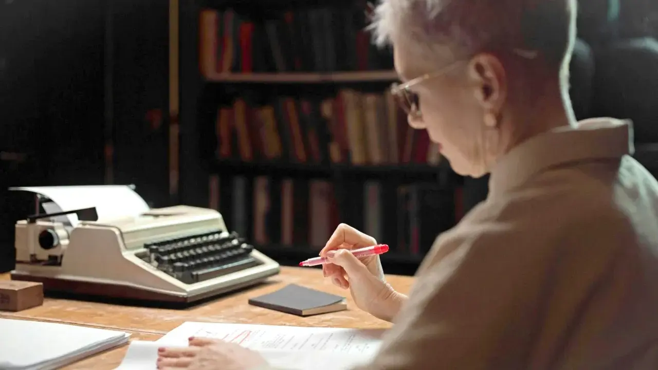 Une femme relit des manuscrits devant une machine à écrire, peut-être pour les éditions Jouvence.