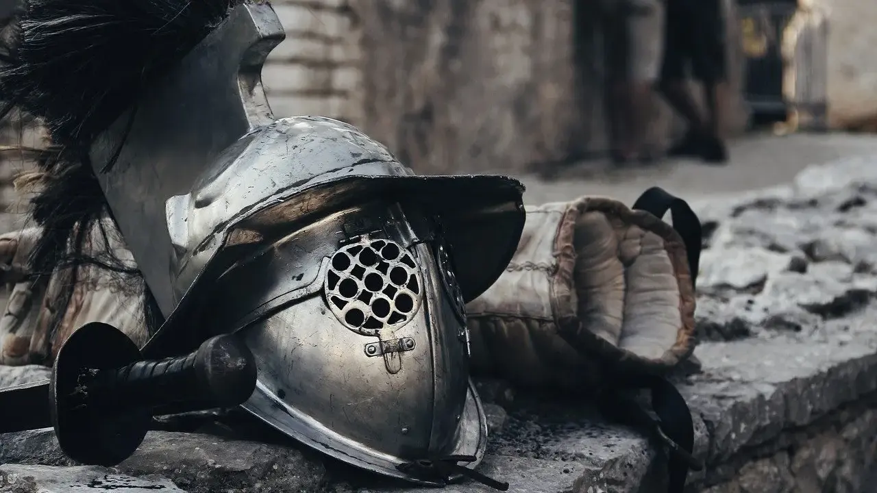 Casque de gladiateur et son épée, rappelant un prénom masculin médiéval fantastique. L'armure repose sur des pierres, prête pour le combat.