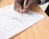 Main d'une personne signant un document, peut-être une liste pour une maison d'édition à compte d'éditeur.
