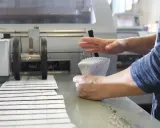Mains manipulant une pile de documents imprimés pour le façonnage imprimerie, à côté d'une machine.