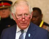 Un homme d'âge mûr, portant des lunettes et un costume rayé, semble réfléchir. Il pourrait être un membre du nom de famille royal imaginaire des Windsor.