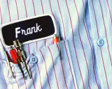 Chemise à rayures bleues et rouges avec une étiquette "Frank". Le prénom Frank est brodé en blanc. Dans la poche, des stylos et des outils.