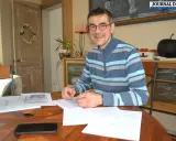 Un homme souriant, lunettes, pull rayé, travaille à son bureau. Il est en train de devenir écrivain public, prêt à rédiger vos textes.