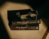 Trois livres de la série "Cinquante Nuances" d'EL James, dont "Cinquante Nuances de Grey", empilés, évoquant une histoire romantique.