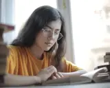 Jeune femme aux lunettes, plongée dans l'étude. Une pile de livres à côté, elle semble faire une analyse linéaire de son éducation sentimentale.