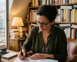 Une femme rédige des manuscrits dans son bureau, entourée de livres. Elle travaille pour une maison d'édition poésie.