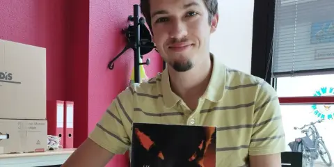 Un jeune écrivain souriant tient son livre "Les Peuples de la Terre".