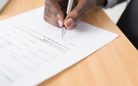 Main d'une personne signant un document, peut-être une liste pour une maison d'édition à compte d'éditeur.