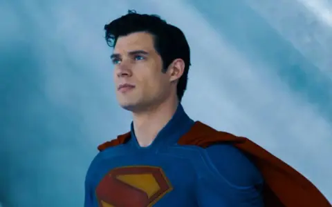 Superman, prénom de héros masculin, regarde au loin, son costume bleu et sa cape rouge flottant.