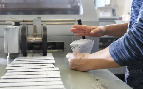 Mains manipulant une pile de documents imprimés pour le façonnage imprimerie, à côté d'une machine.