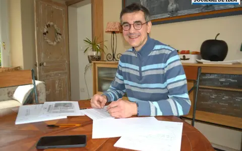 Un homme souriant, lunettes, pull rayé, travaille à son bureau. Il est en train de devenir écrivain public, prêt à rédiger vos textes.
