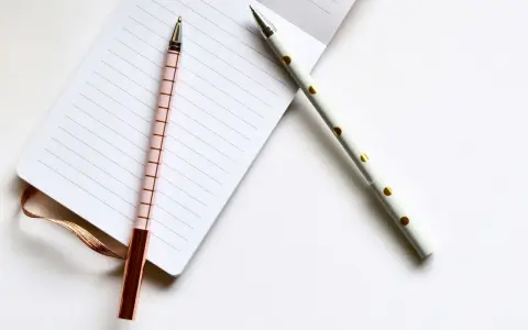 Deux stylos élégants, un rose à carreaux et un blanc à pois dorés, reposent sur un carnet ligné, prêts pour les éditions Balland manuscrit.