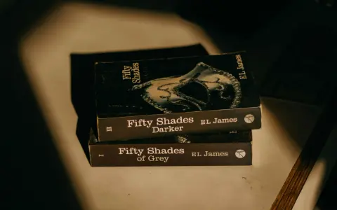 Trois livres de la série "Cinquante Nuances" d'EL James, dont "Cinquante Nuances de Grey", empilés, évoquant une histoire romantique.