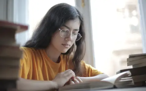 Jeune femme aux lunettes, plongée dans l'étude. Une pile de livres à côté, elle semble faire une analyse linéaire de son éducation sentimentale.