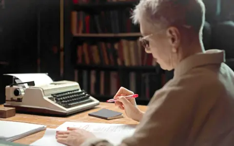 Une femme relit des manuscrits devant une machine à écrire, peut-être pour les éditions Jouvence.
