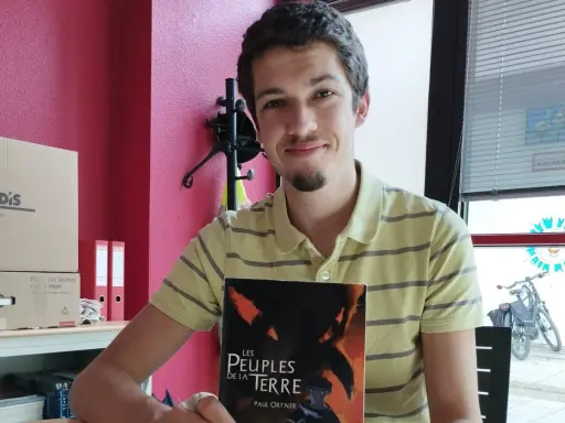 Un jeune écrivain souriant tient son livre "Les Peuples de la Terre".