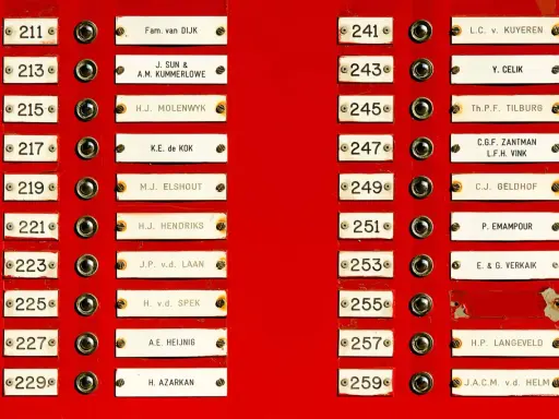 Plaque de sonnette rouge avec des noms de famille, comme "Fam. van DIJK" ou "L.C. v. KUYEREN". Une idée de nom de famille français pourrait être "Leclair".