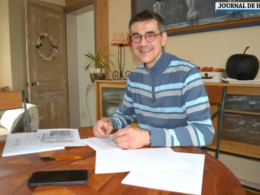 Un homme souriant, lunettes, pull rayé, travaille à son bureau. Il est en train de devenir écrivain public, prêt à rédiger vos textes.