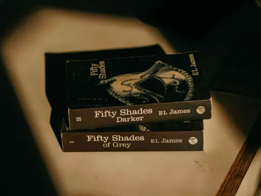 Trois livres de la série "Cinquante Nuances" d'EL James, dont "Cinquante Nuances de Grey", empilés, évoquant une histoire romantique.