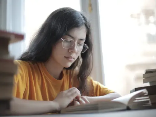 Jeune femme aux lunettes, plongée dans l'étude. Une pile de livres à côté, elle semble faire une analyse linéaire de son éducation sentimentale.