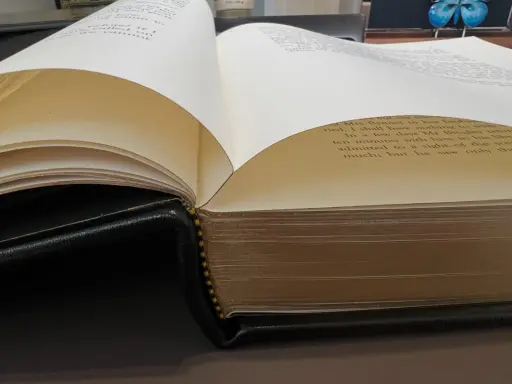 Gros plan sur des pages de livre ouvertes, révélant le texte imprimé et la reliure en cuir noir.