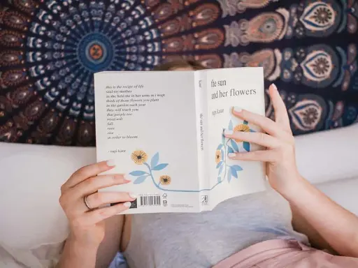 Une personne lit "the sun and her flowers" de Rupi Kaur, un livre de poésie. La dernière page d'un livre s'appelle la postface.