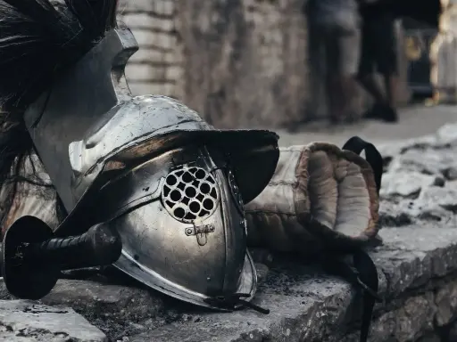 Casque de gladiateur et son épée, rappelant un prénom masculin médiéval fantastique. L'armure repose sur des pierres, prête pour le combat.