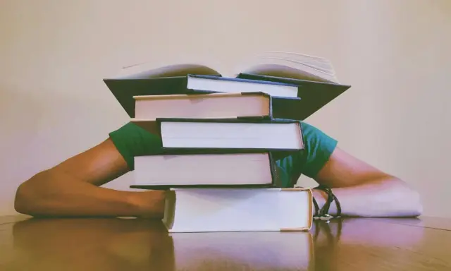 Une pile de livres sur la tête, symbolisant le poids de la connaissance et le sujet philo conscience.