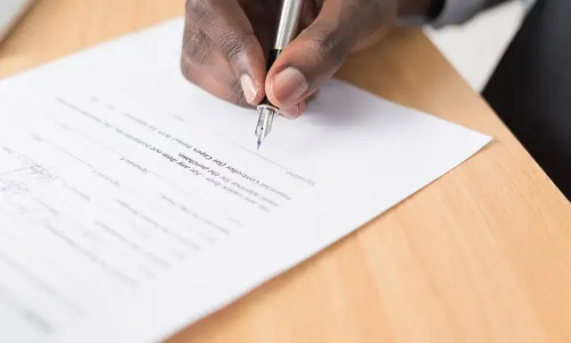 Main d'une personne signant un document, peut-être une liste pour une maison d'édition à compte d'éditeur.