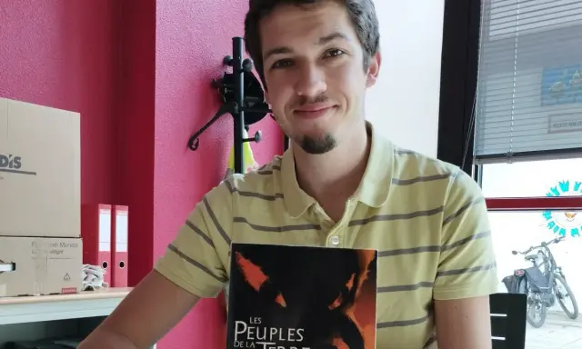 Un jeune écrivain souriant tient son livre "Les Peuples de la Terre".