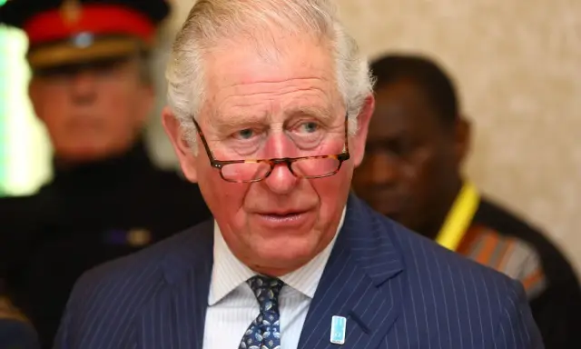 Un homme d'âge mûr, portant des lunettes et un costume rayé, semble réfléchir. Il pourrait être un membre du nom de famille royal imaginaire des Windsor.