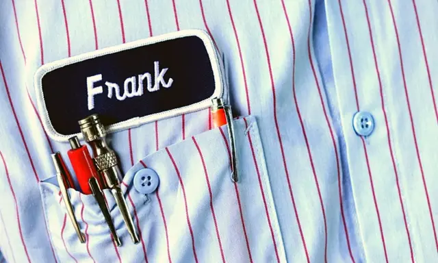 Chemise à rayures bleues et rouges avec une étiquette "Frank". Le prénom Frank est brodé en blanc. Dans la poche, des stylos et des outils.