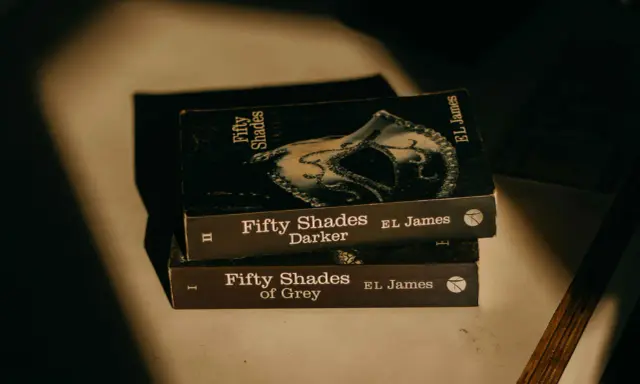 Trois livres de la série "Cinquante Nuances" d'EL James, dont "Cinquante Nuances de Grey", empilés, évoquant une histoire romantique.