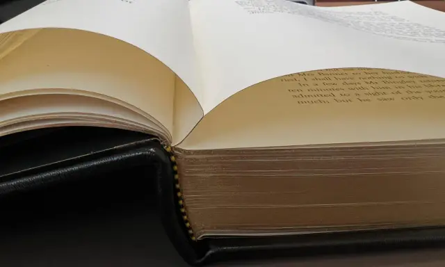 Gros plan sur des pages de livre ouvertes, révélant le texte imprimé et la reliure en cuir noir.