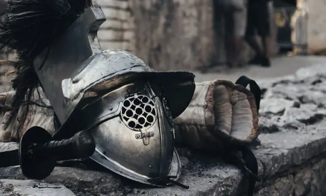 Casque de gladiateur et son épée, rappelant un prénom masculin médiéval fantastique. L'armure repose sur des pierres, prête pour le combat.