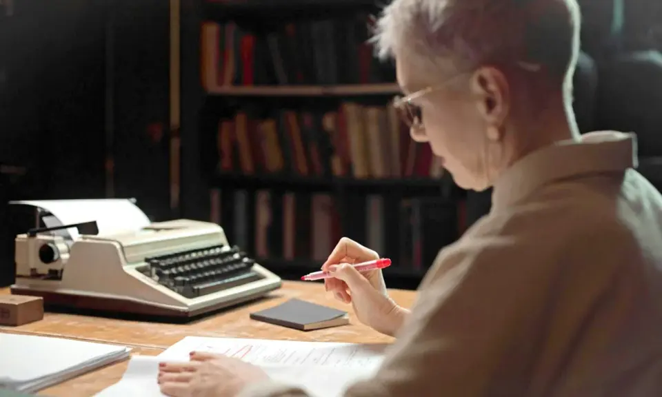 Une femme relit des manuscrits devant une machine à écrire, peut-être pour les éditions Jouvence.