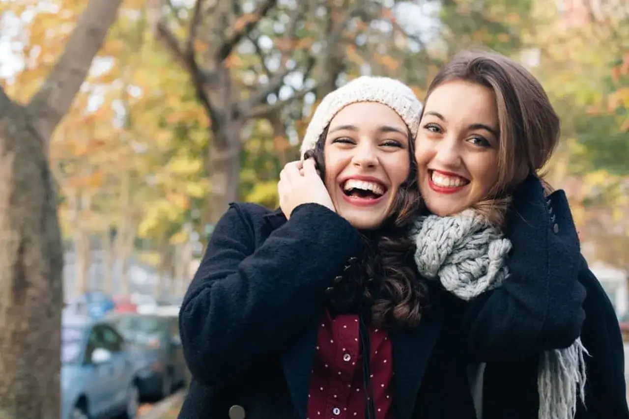 Deux amies rient aux &eacute;clats, bras dessus, bras dessous, sous les arbres d'automne. Une belle histoire d'amiti&eacute;.