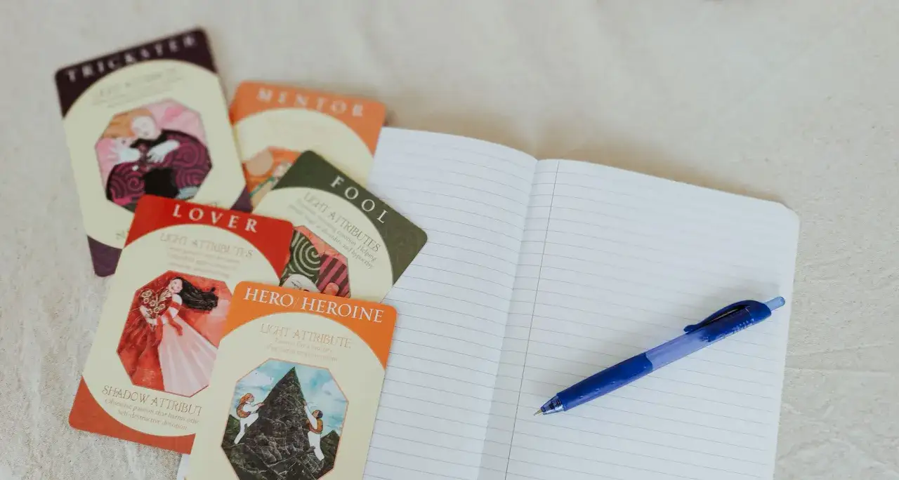 Cartes d'archétypes (Trickster, Mentor, Lover, Fool, Hero/Heroine) près d'un carnet ouvert et d'un stylo. Le nom