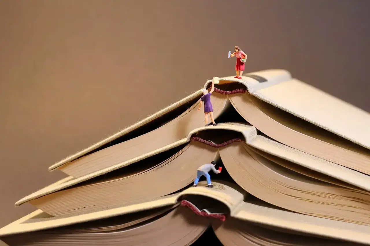 Trois figurines s'activent sur des livres ouverts, comme pour publier un livre. L'une tient un livre, une autre semble &eacute;crire.